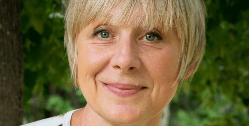 En kvinna med blont hår ler mot kameran.