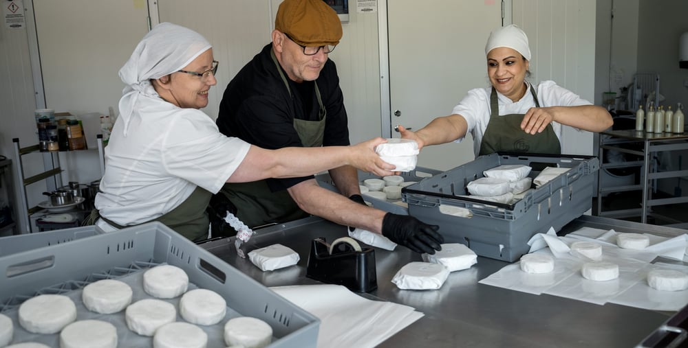 Tre vuxna personer packar ost i köksmiljö.