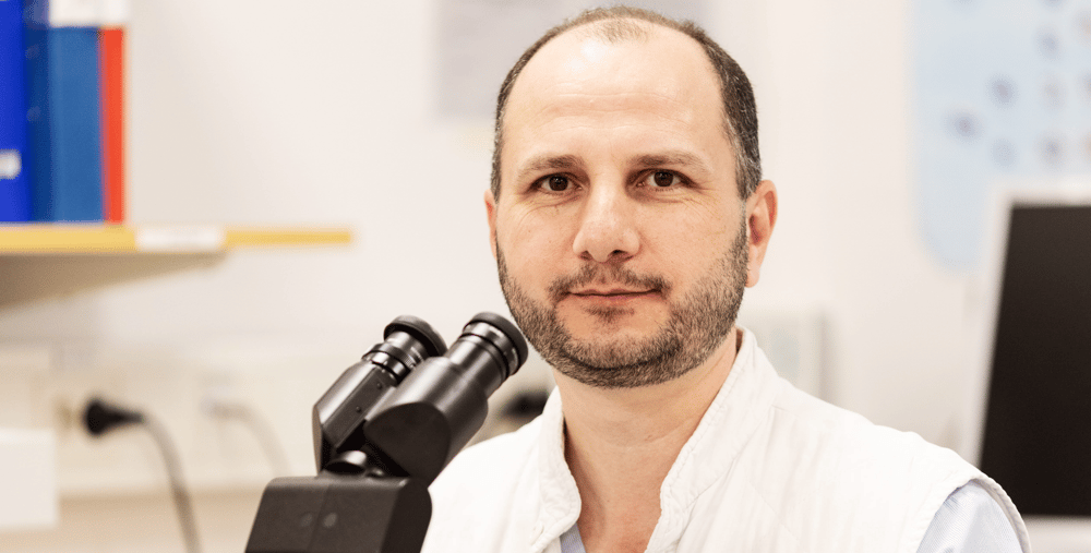 En man sitter vid ett bord framför ett mikroskop.