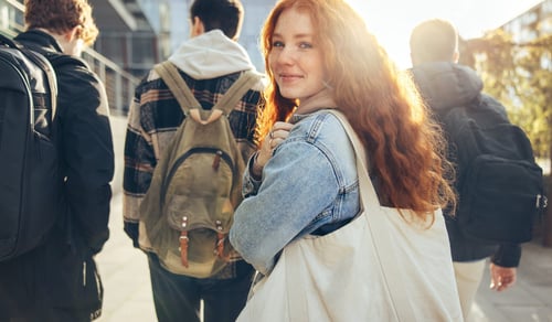 Female student glancing back while going for a class in college. Girl walking with friends going for class in high school.