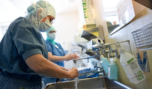 Två läkare i operationskläder tvättar händerna i ett handfat.