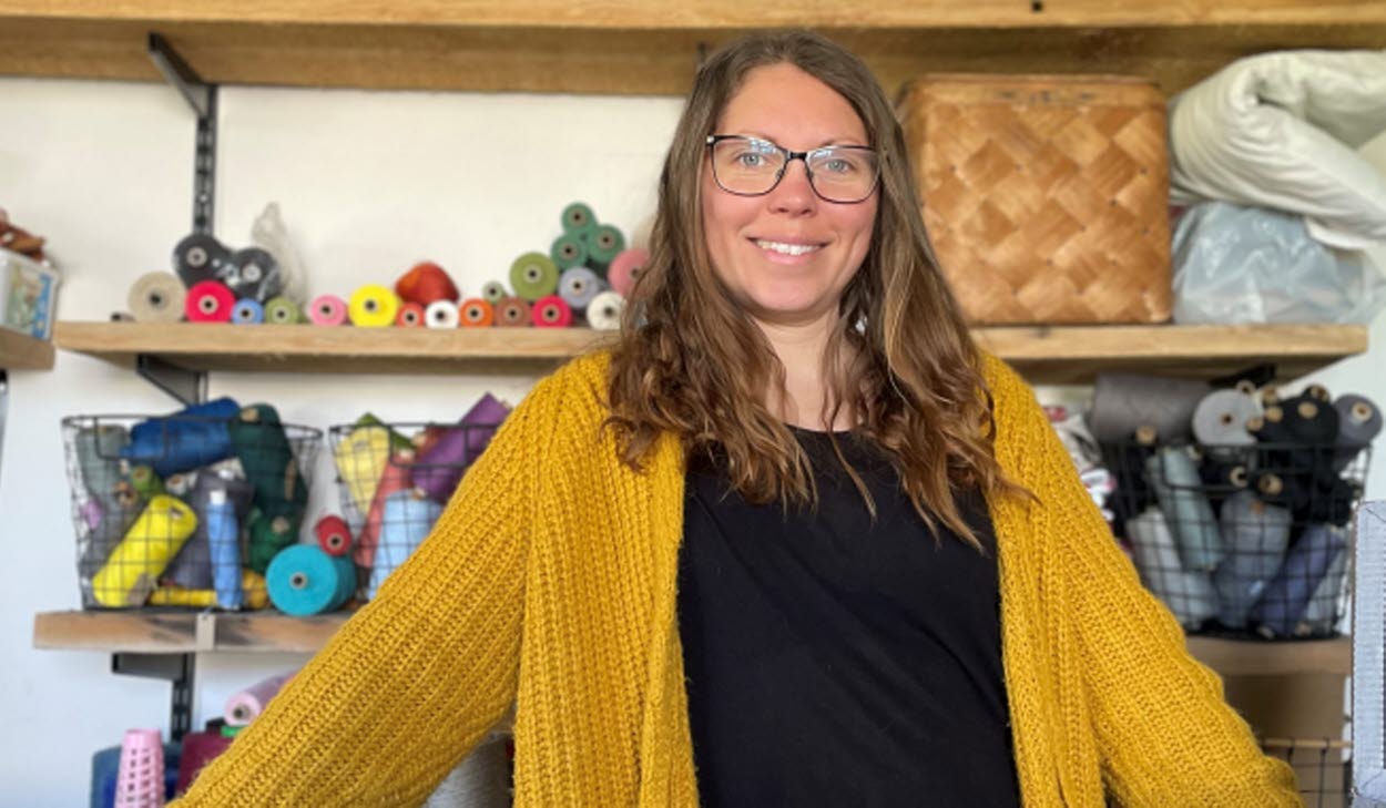 Person som står framför hyllor med tyger och vävverktyg