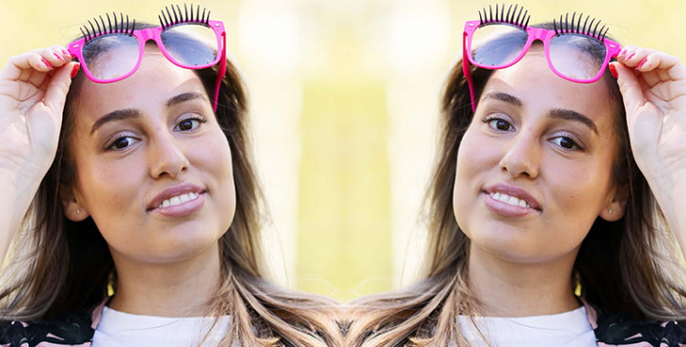 Person tittande in i kameran hållande ett par rosa solglasögon ovanför sitt huvud