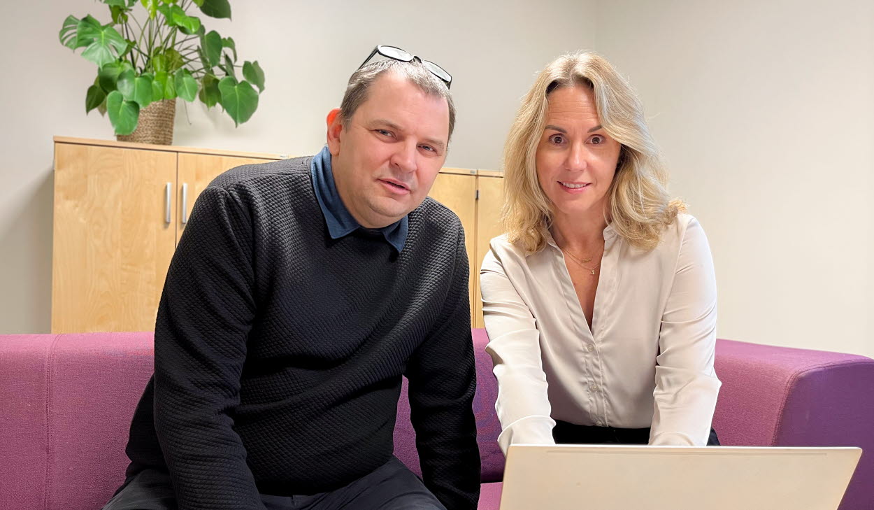 Sam Cole och Malin Schönning sitter i en vinröd soffa med en dator framför sig på ett bord. 