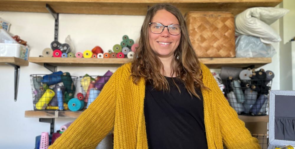 Person som står framför hyllor med tyger och vävverktyg